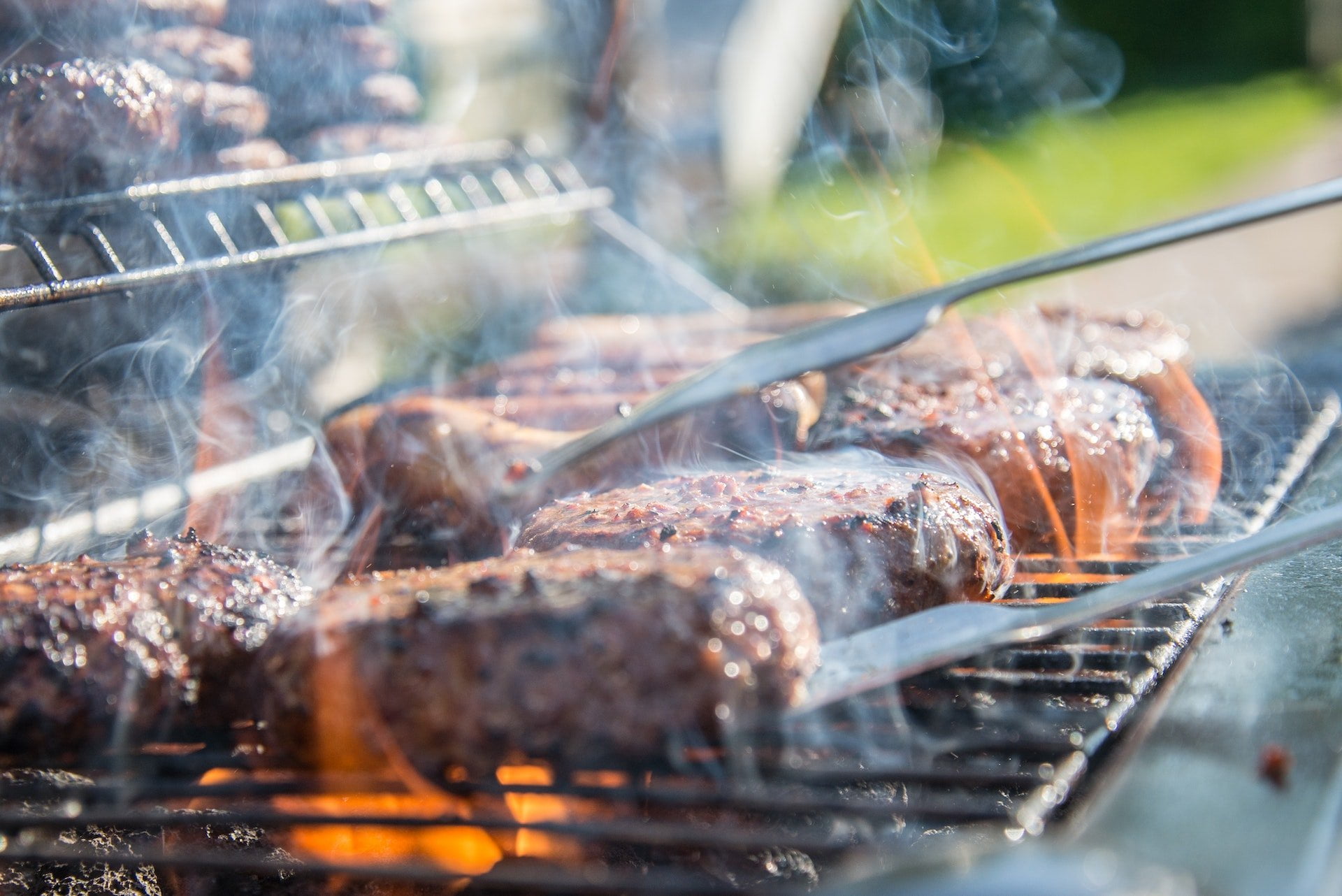 pexels-skitterphoto-1105325 Close-up of several burgers grilling on an outdoor barbecue, with smoke rising and tongs flipping one of them—much like how a pressure washing company revitalizes surfaces with their precision technique.