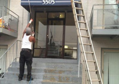 condo exteriors A person from a pressure washing company is power washing the entrance and stairs of a building under the sign "5505," with a ladder leaning against the facade.
