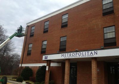 A person operates a lift to clean the exterior of the Metropolitan building, Dr. H. Beecher Hicks, Jr. Senior Servant, using professional pressure cleaning services from a top-rated Pressure Washing Company.