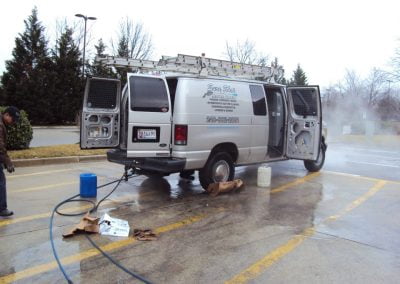 A van with open doors and ladders on top is being pressure washed in a parking lot by a professional Pressure Washing Company.