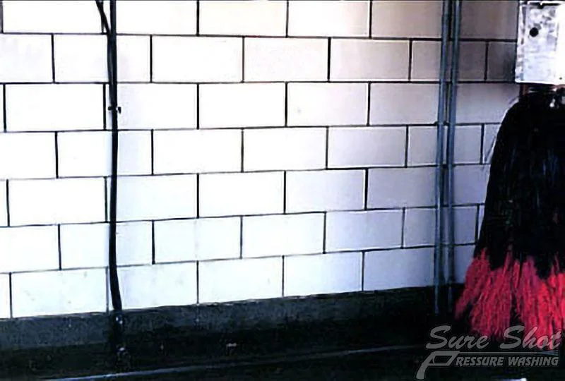 A brick wall at a car wash, with part of a red and black brush visible to the right side, showcases the effective tools used by our Pressure Washing Company.