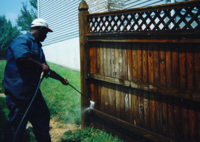 A person pressure washing a wooden fence, representing "Sure Shot Pressure Washing Company," with their logo in the bottom right corner.