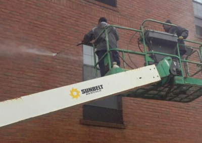 Two workers on a lift pressure washing the side of a brick building. The "Sure Shot Pressure Washing Company" logo is prominently displayed on the image, showcasing their professional pressure cleaning services.